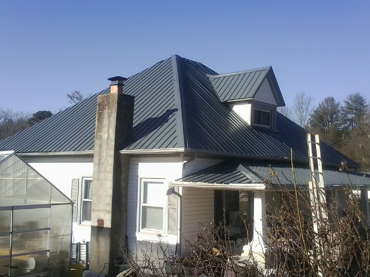 Dark blue standing seam metal roof on a white farmhouse with dormer — Slate & Tile Roof Repair by Roofing Brothers in Elkin