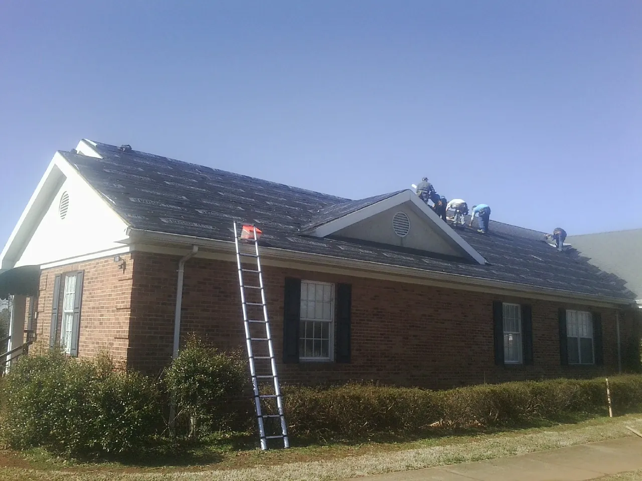 Crew tearing shingles off a brick ranch roof with a ladder set — Emergency Roof Repair work by our crew in Elkin