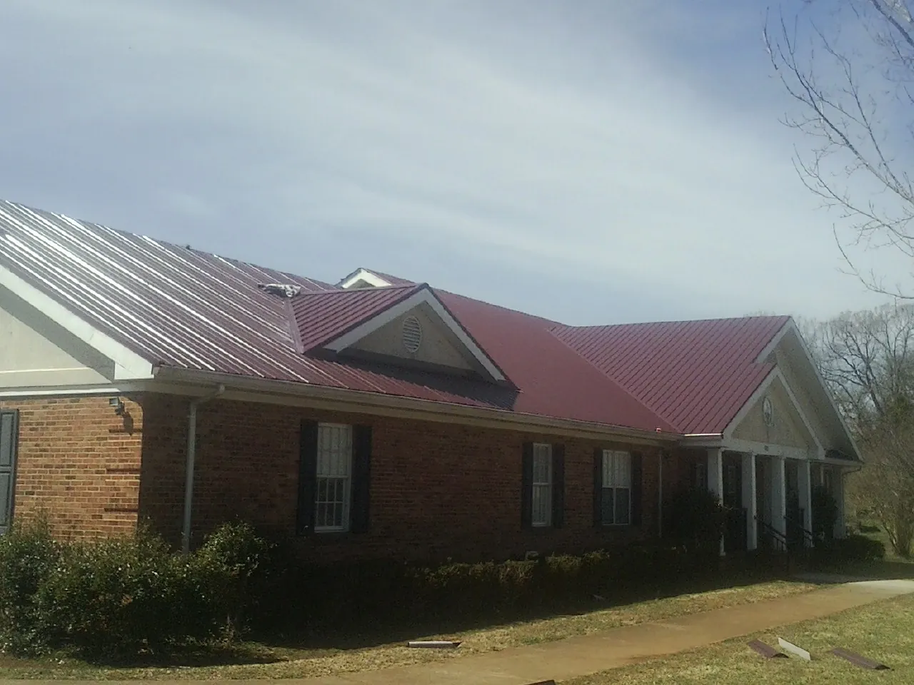 Red metal roof with gabled entries on a long brick building, from a Hail Damage Roof Repair job in Elkin