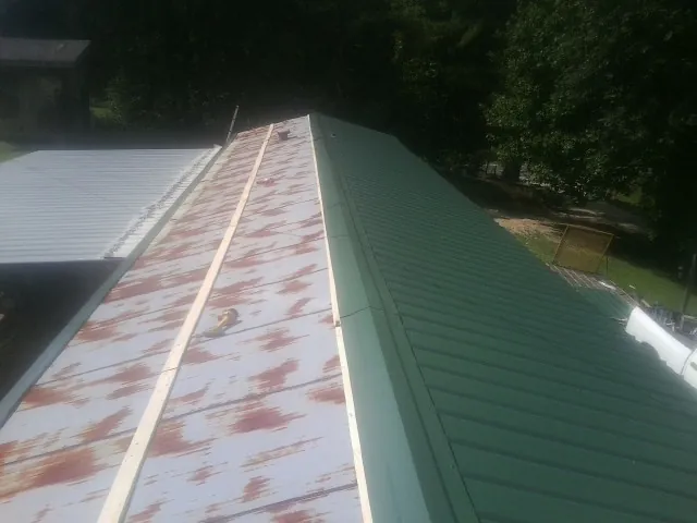 Old rusted panels beside newly installed green metal roofing — Wind Damage Roof Repair by Roofing Brothers in Elkin