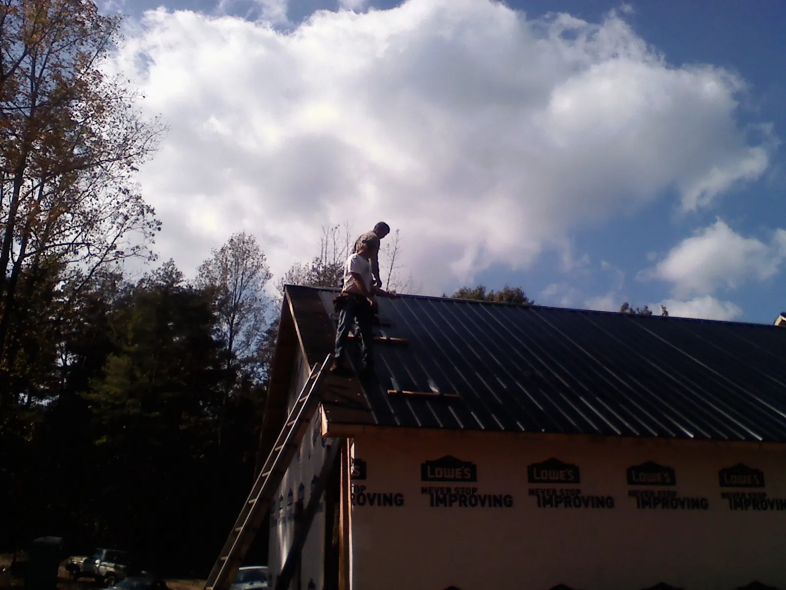 Roofer fastening dark metal panels high against a cloudy sky, from a Roof Inspection job in Elkin