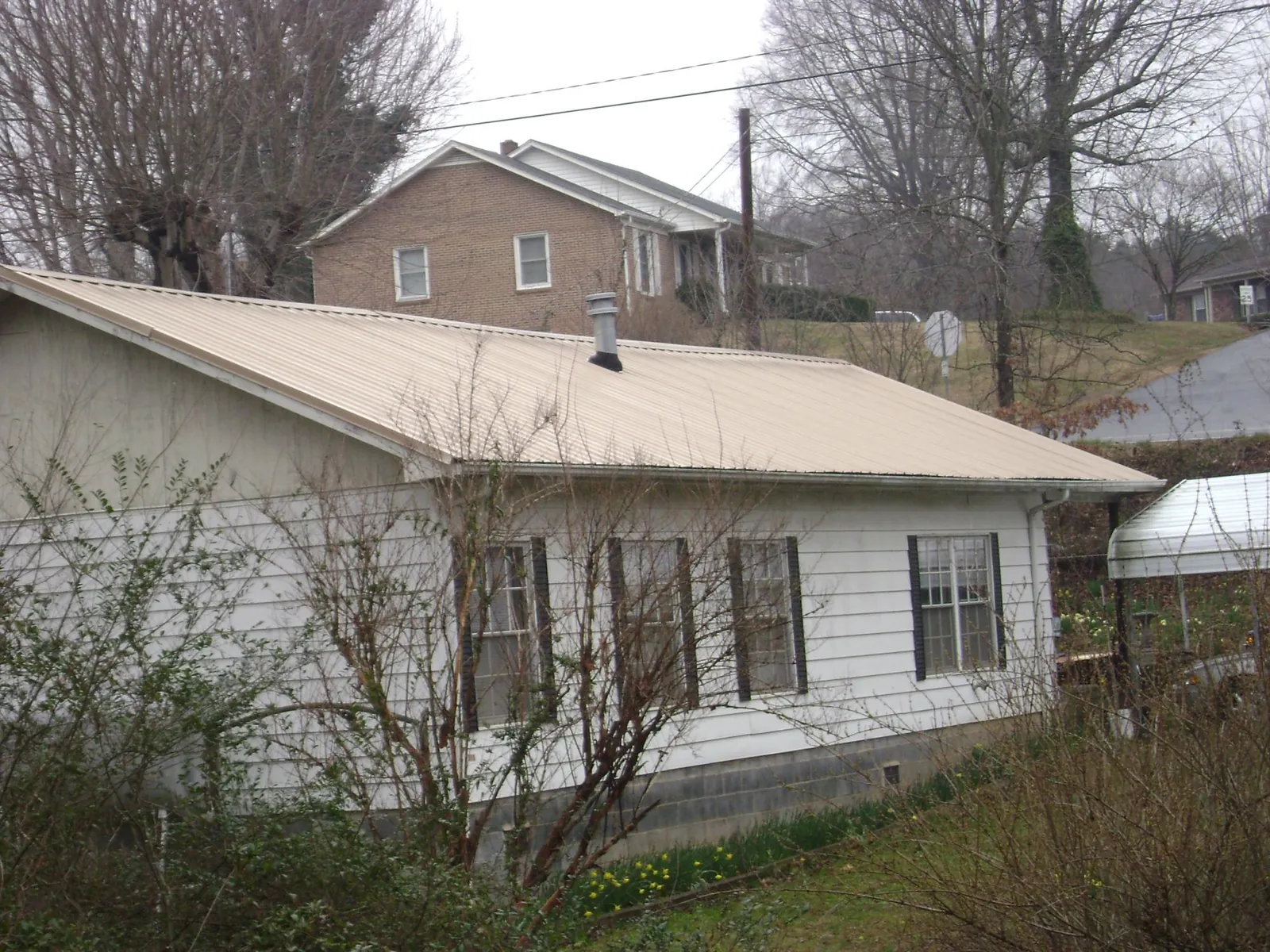 Tan metal roof on a white sided house set into a hillside — Commercial Roofing by Roofing Brothers in Elkin