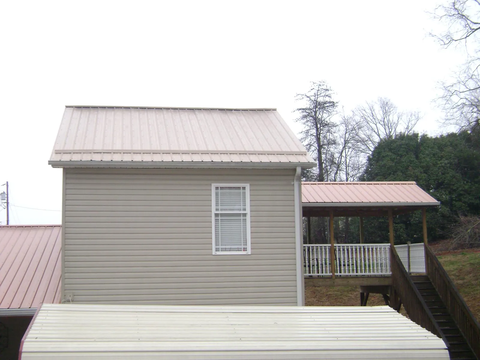 Tan metal roofs on a two story addition and attached porch, from a Roof Replacement job in Elkin